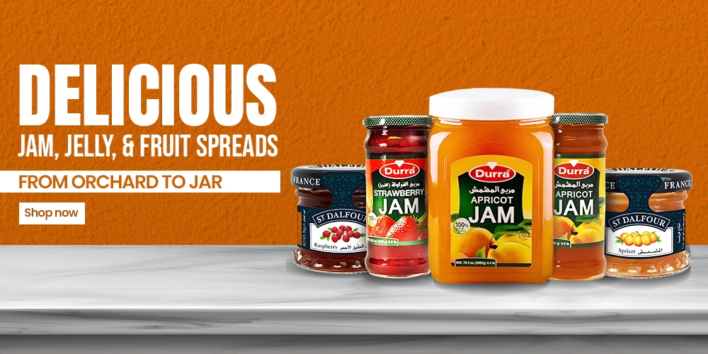 Assorted fruit spreads on a marble counter against an orange backdrop, featuring Durra apricot and strawberry jams with St. Dalfour jars.
